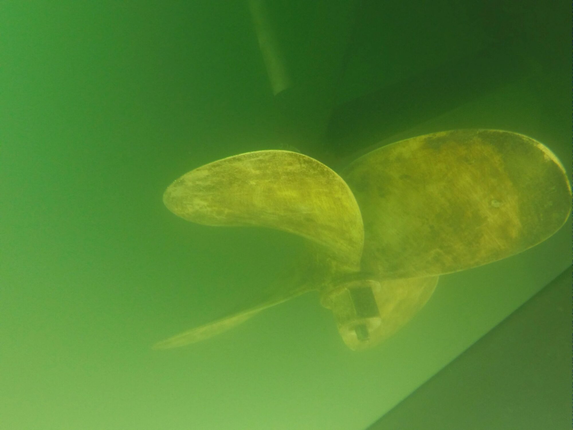 Underwater view of a freshly serviced bronze propeller and zinc beneath a boat hull