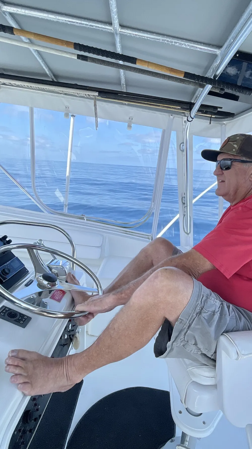 Brett at the helm of Merityme III, hand on the wheel, open water astern